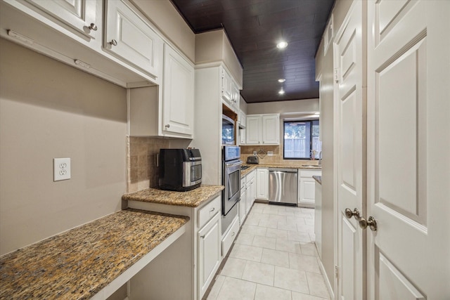 kitchen with white cabinetry, stainless steel appliances, backsplash, stone countertops, and light tile patterned flooring