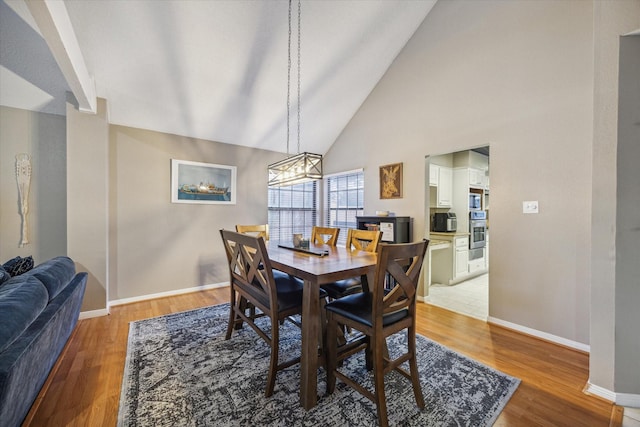 dining area with light wood-type flooring, high vaulted ceiling, and a chandelier