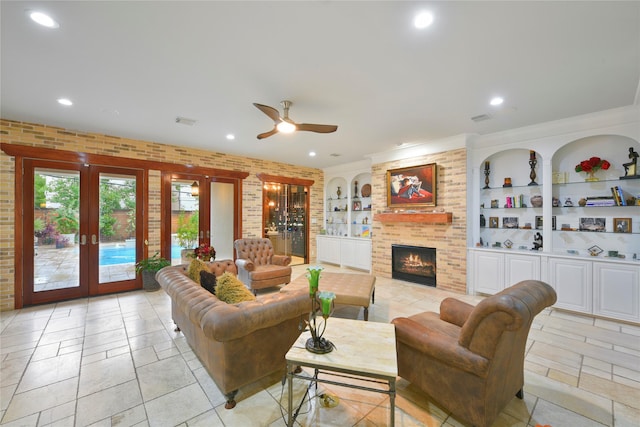 living room featuring french doors, brick wall, built in shelves, ceiling fan, and a fireplace