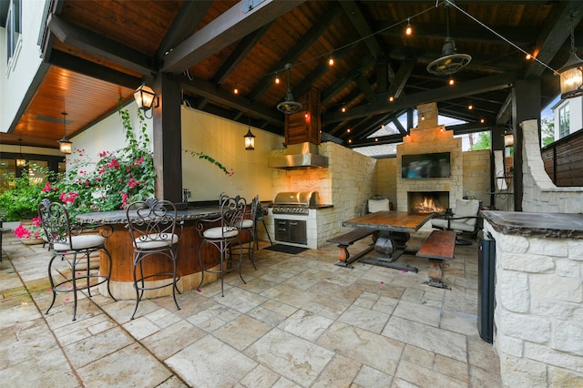 view of patio / terrace featuring an outdoor stone fireplace, a grill, exterior bar, and an outdoor kitchen