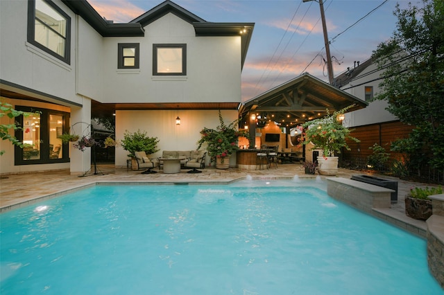 pool at dusk featuring an outdoor living space with a fireplace, pool water feature, and a patio area