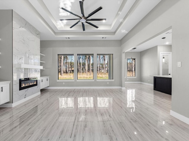 unfurnished living room featuring a tile fireplace, ceiling fan, built in shelves, a raised ceiling, and light hardwood / wood-style floors