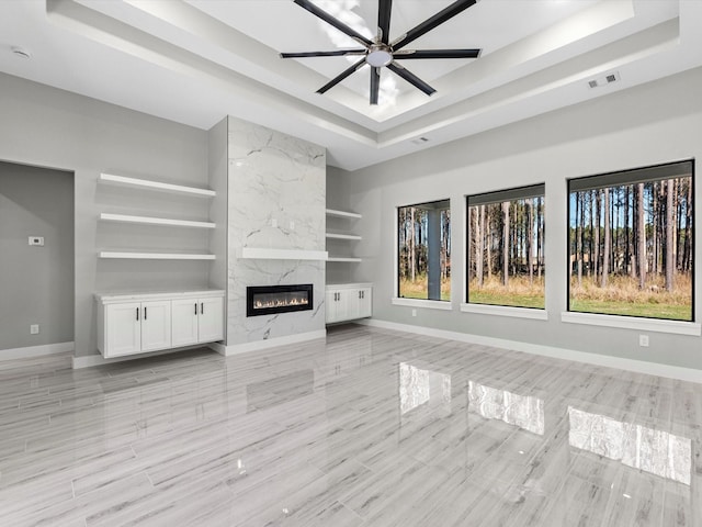 unfurnished living room with a tray ceiling, ceiling fan, and a premium fireplace