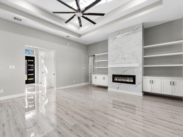 unfurnished living room with a high end fireplace, built in shelves, a tray ceiling, and ceiling fan