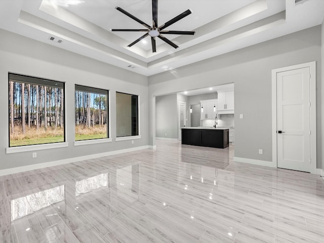 unfurnished living room with ceiling fan, a raised ceiling, and sink