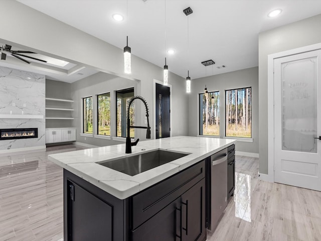 kitchen featuring built in shelves, sink, light stone counters, decorative light fixtures, and a center island with sink