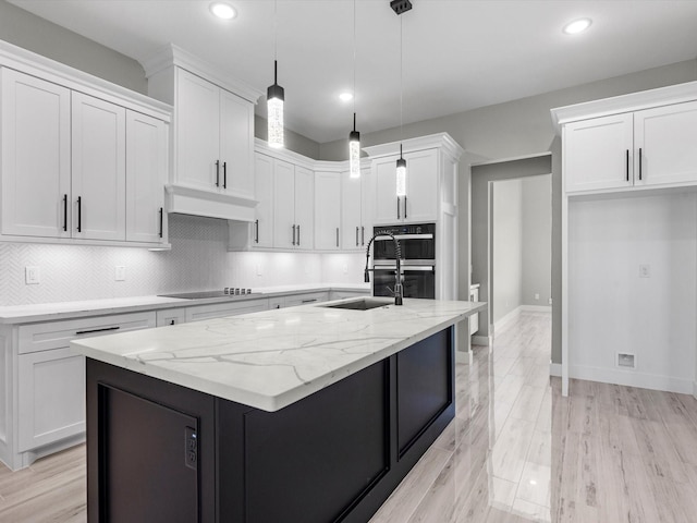 kitchen featuring light stone counters, custom range hood, a kitchen island with sink, white cabinets, and hanging light fixtures