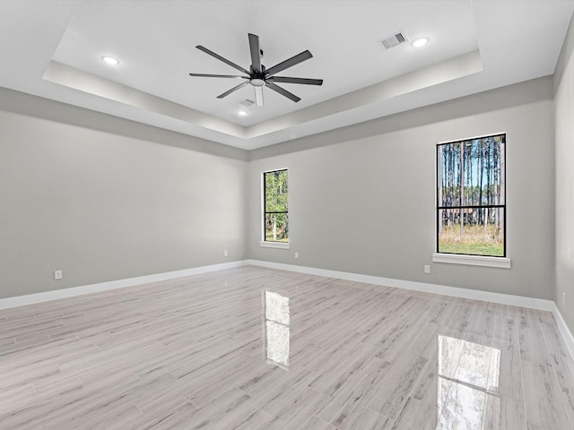 spare room with ceiling fan, a raised ceiling, and light wood-type flooring