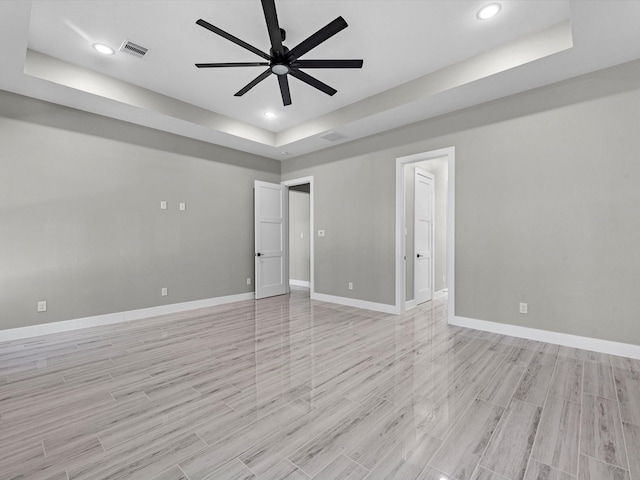 empty room featuring a raised ceiling, ceiling fan, and light hardwood / wood-style flooring