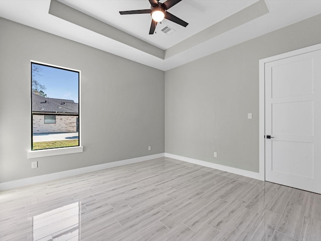 empty room featuring ceiling fan, a healthy amount of sunlight, and a tray ceiling