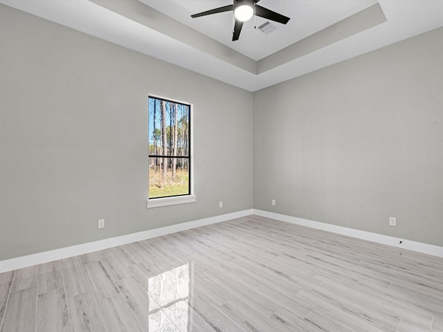 spare room with ceiling fan, light wood-type flooring, and a tray ceiling