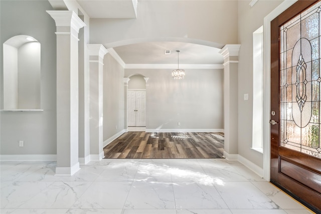 entryway featuring a notable chandelier, crown molding, and decorative columns