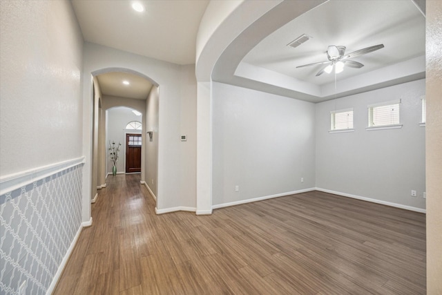 empty room featuring wood-type flooring, a raised ceiling, ceiling fan, and a healthy amount of sunlight