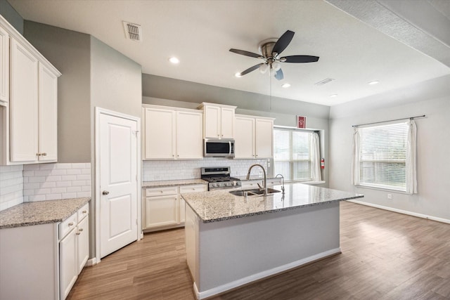 kitchen featuring white cabinets, appliances with stainless steel finishes, light stone counters, and sink