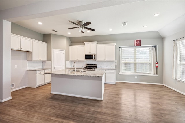 kitchen with a kitchen island with sink, sink, appliances with stainless steel finishes, light stone counters, and white cabinetry