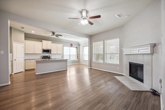 unfurnished living room with wood-type flooring, sink, ceiling fan, and a tiled fireplace