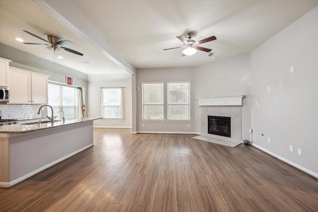 unfurnished living room with a fireplace, dark hardwood / wood-style floors, ceiling fan, and sink