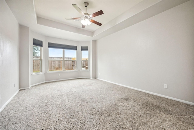 carpeted empty room featuring ceiling fan and a raised ceiling