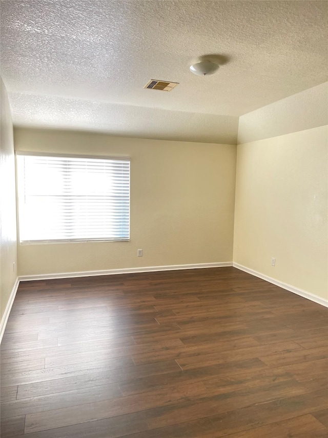 empty room featuring a textured ceiling, vaulted ceiling, and dark wood-type flooring