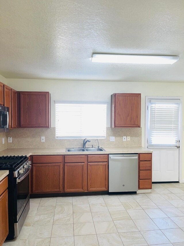 kitchen with a textured ceiling, light tile patterned floors, sink, and appliances with stainless steel finishes