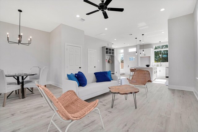 living room with ceiling fan with notable chandelier, light hardwood / wood-style floors, and sink