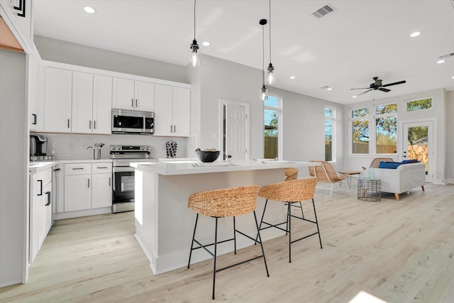 kitchen featuring pendant lighting, white cabinets, light hardwood / wood-style flooring, a kitchen island, and stainless steel appliances