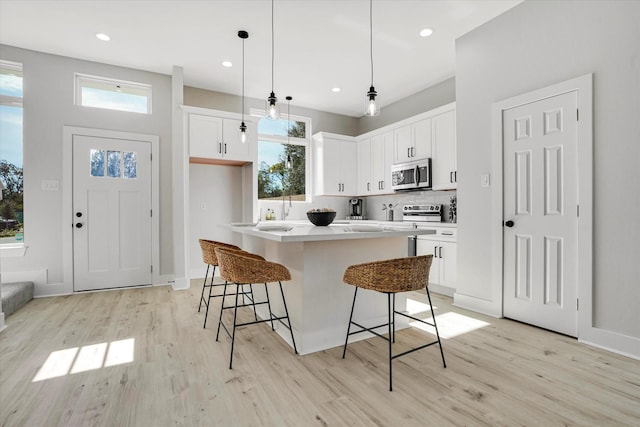 kitchen featuring white cabinets, light hardwood / wood-style floors, appliances with stainless steel finishes, decorative light fixtures, and a kitchen island