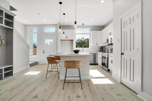 kitchen with white cabinetry, a center island, light hardwood / wood-style floors, pendant lighting, and appliances with stainless steel finishes