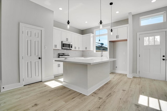 kitchen with stainless steel appliances, white cabinets, light hardwood / wood-style floors, a kitchen island, and hanging light fixtures