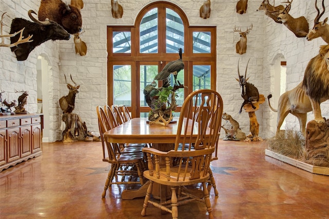 dining room featuring concrete flooring, a towering ceiling, and french doors