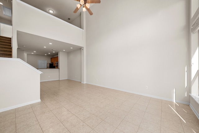 unfurnished living room with ceiling fan, a towering ceiling, and light tile patterned floors