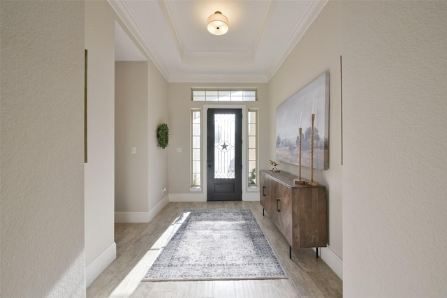 entryway with light wood-style floors, baseboards, a raised ceiling, and crown molding