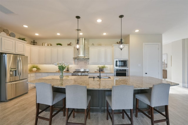 kitchen featuring a large island with sink, pendant lighting, wall chimney exhaust hood, and stainless steel appliances