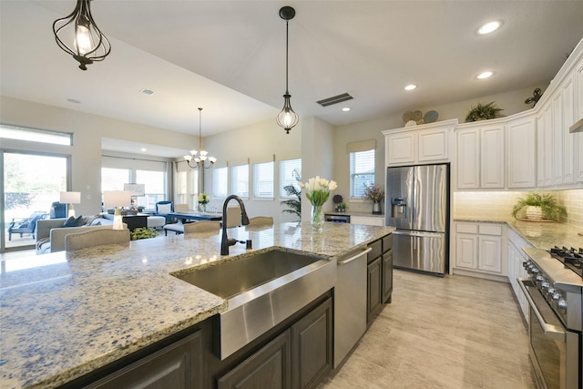 kitchen with an inviting chandelier, sink, light stone countertops, appliances with stainless steel finishes, and white cabinetry