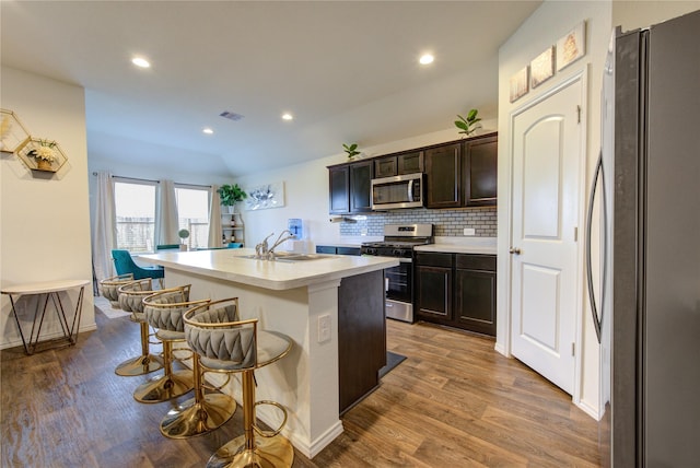 kitchen featuring a kitchen bar, appliances with stainless steel finishes, sink, a center island with sink, and hardwood / wood-style flooring