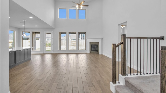 unfurnished living room with recessed lighting, a glass covered fireplace, ceiling fan, wood finished floors, and baseboards