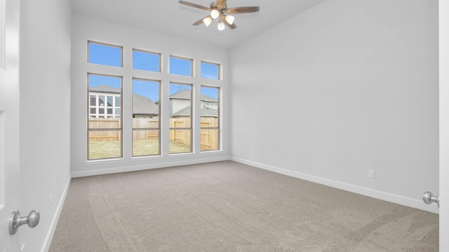 carpeted spare room featuring a towering ceiling, a ceiling fan, and baseboards