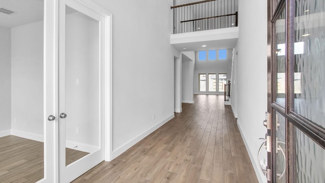 hallway with french doors, a high ceiling, wood finished floors, and visible vents