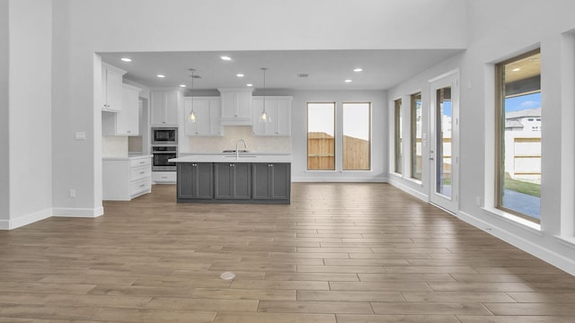 kitchen featuring light wood finished floors, appliances with stainless steel finishes, open floor plan, white cabinetry, and a sink