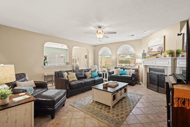 living room featuring a tile fireplace, light tile patterned floors, a textured ceiling, and ceiling fan