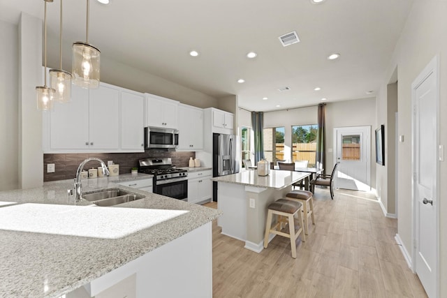 kitchen featuring appliances with stainless steel finishes, a kitchen island, sink, pendant lighting, and white cabinetry