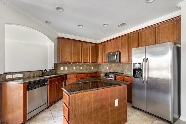 kitchen with a center island, dark stone counters, light tile patterned floors, ornamental molding, and stainless steel appliances