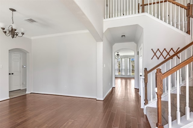 entrance foyer with ceiling fan with notable chandelier, ornamental molding, dark wood-type flooring, and a high ceiling