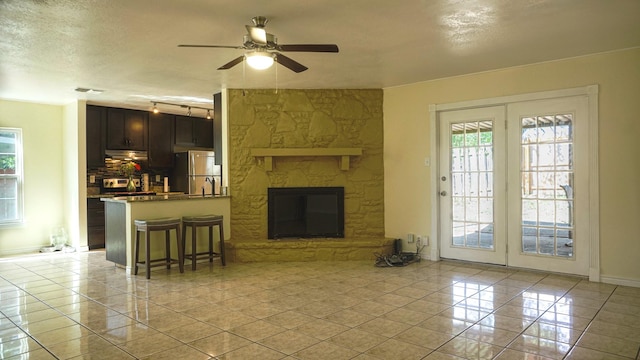 tiled living room with a fireplace, a textured ceiling, and ceiling fan