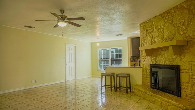 unfurnished living room with a fireplace, light tile patterned floors, a textured ceiling, and ceiling fan