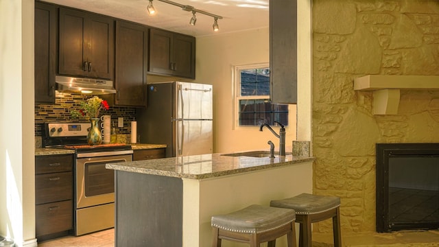 kitchen with light stone countertops, a kitchen breakfast bar, dark brown cabinets, stainless steel appliances, and sink