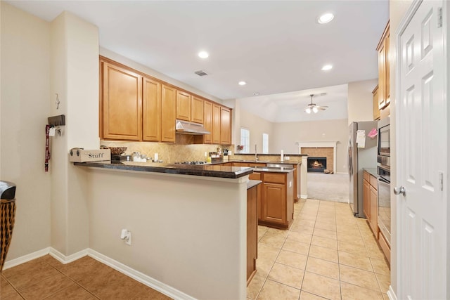 kitchen featuring ceiling fan, sink, stainless steel appliances, kitchen peninsula, and a tiled fireplace