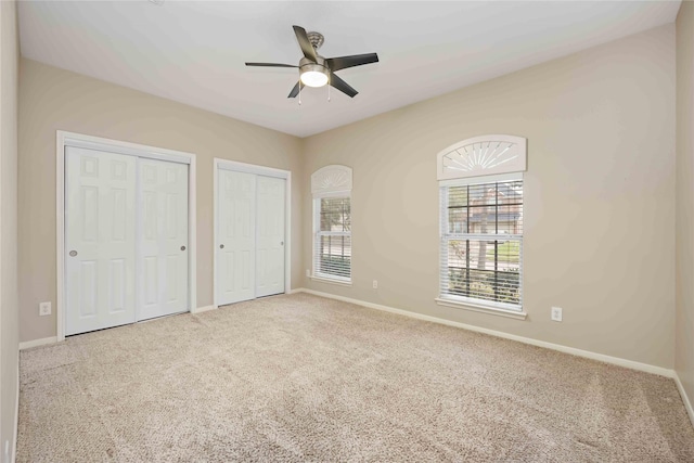 unfurnished bedroom with ceiling fan, light colored carpet, and two closets