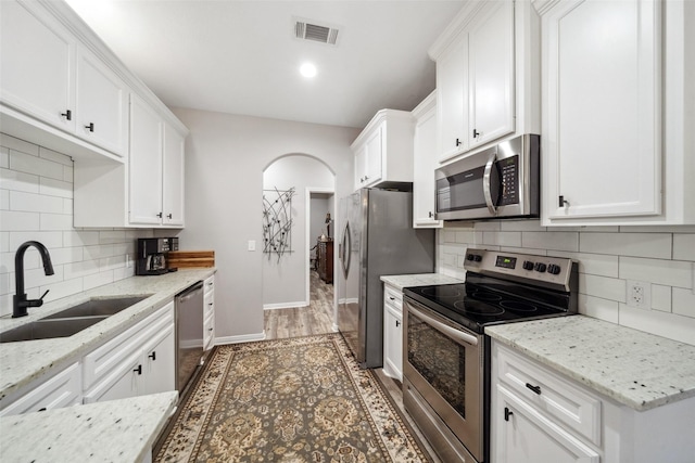 kitchen with sink, light stone counters, backsplash, white cabinets, and appliances with stainless steel finishes