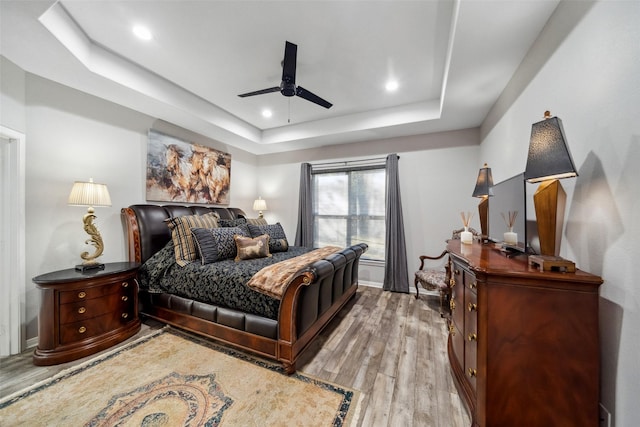 bedroom with ceiling fan, light hardwood / wood-style floors, and a raised ceiling